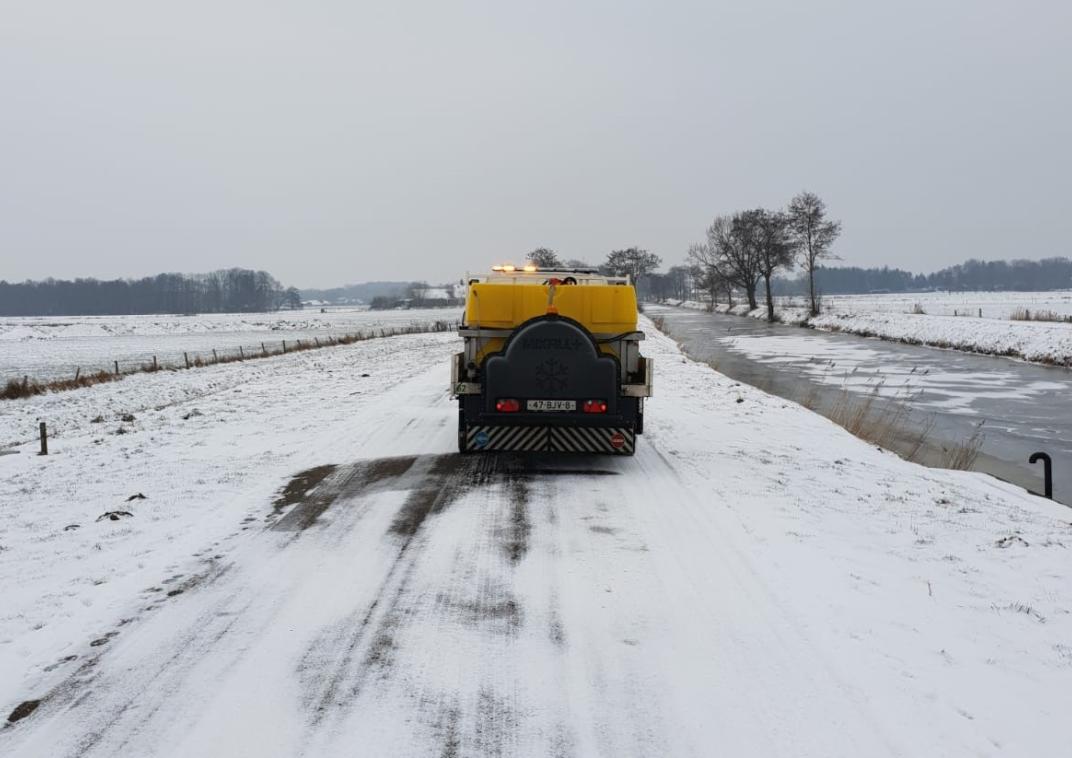 Strooiwagen op een witbesneeuwde weg langs diep